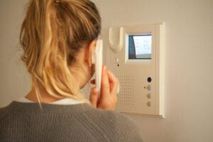 Frau, die einen Anruf an einer Türsprechanlage entgegennimmt, während sie auf den Bildschirm auf dem CRT-Display der Video-Gegensprechanlage blickt